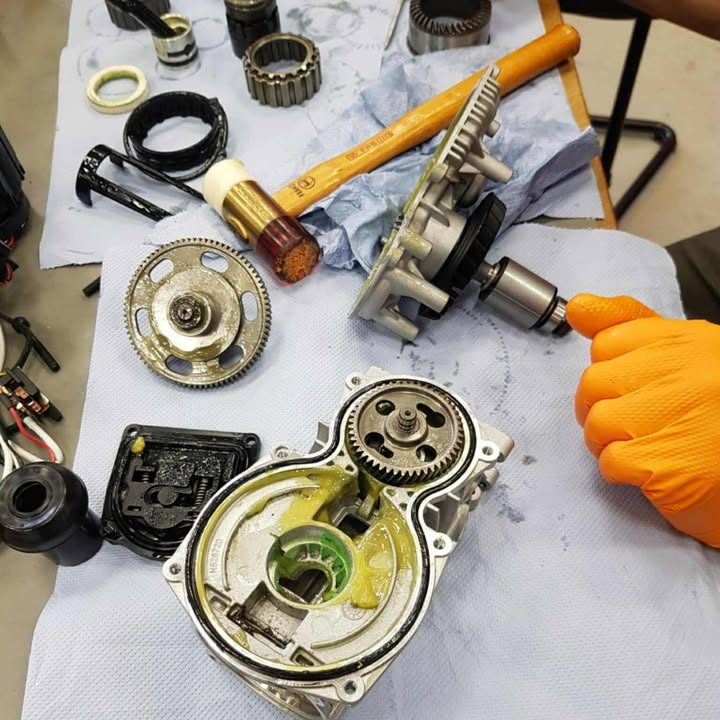 Componente de motor dezasamblate pe o suprafață de lucru, cu o mână care ține o unealtă. Componente de motor dezasamblate pe o suprafață de lucru, cu o mână care ține o unealtă.